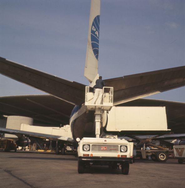 International Harvester Scout with a lift platform at an airport. A man is standing on the platform to inspect the tail of a Pan American World Airways Boeing 747.
