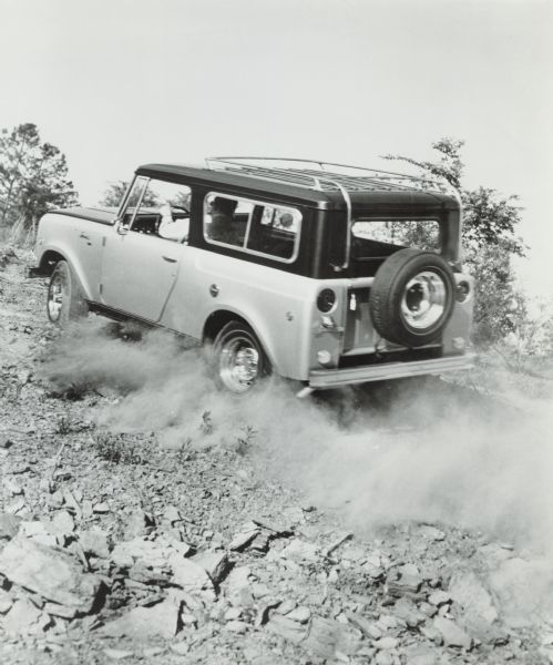 A man is driving an International Scout "limited edition" Aristocrat up a rocky hill. The spare tire is mounted on the back.