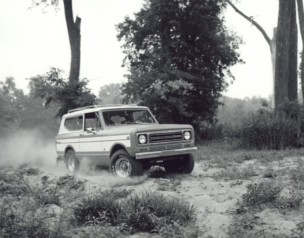 A man is driving an International Harvester Scout II on a sandy road with trees in the background.
