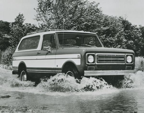 An International Scout Traveler driven through water at the edge of a shoreline, probably across a river.