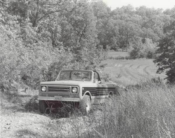 A man is driving an International Scout Terra on a hill in a wooded area. Photograph was taken by International Harvester for Brandt & Assoc., Ltd. Photography of Barrington Hills, Illinois.