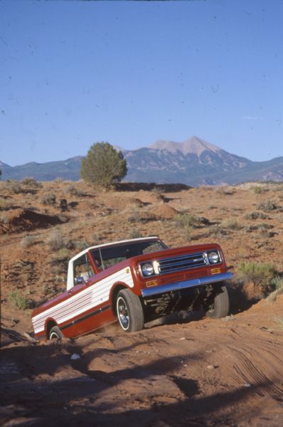 A red and white International Scout II off-roading up a steep rise in the desert.