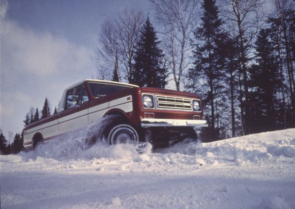 Low angle view of a red and white International Scout Terra being driven through deep snow.