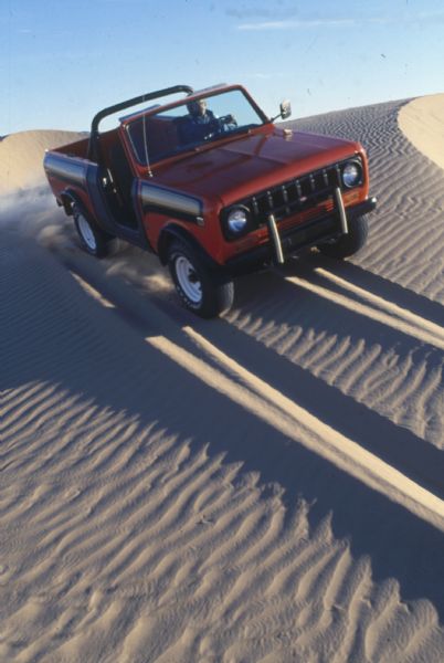 A man drives a red International Scout SS II down a steep sand dune.