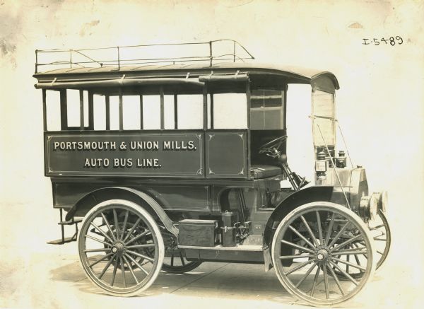 Side view from front of the left side of an International bus used by the Portsmouth & Union Mills Auto Bus Line. There is a luggage rack on the roof.
