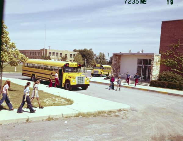 Color photograph of International school buses with Superior brand bodies parked alongside a sidewalk in front of Bath High School in the Eagle Point School District. The buses are a 1603 (steel hood) and 1703 (fiberglass hood). Students are walking and running nearby.