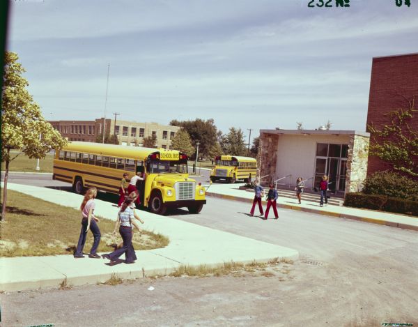 Color photograph of two International 1703 conventional school buses parked near Bath High School (?) in Eagle Point School District. Students are walking nearby.