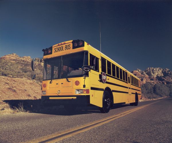 Color photograph of an International school bus parked on a road in a desert setting. The bus driver is barely visible through the front windshield. This image was probably taken for advertisement materials.
