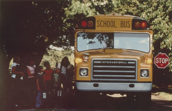 Children are pictured boarding a S-Series International school bus. The color photograph was probably taken for advertising purposes.