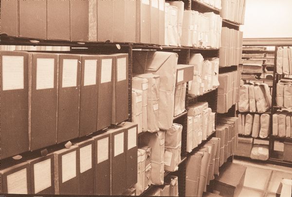 Storage shelves in the stacks of the Wisconsin Historical Society Archives show the papers of the McCormick Collection housed in boxes and paper wrapped bundles tied with string.