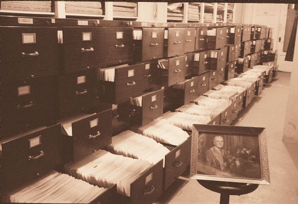 A line of filing cabinets holding the Anita McCormick Blaine papers, not long after they arrived at the Wisconsin Historical Society in the 1950s. A portrait of Anita is displayed on a stool in front of the cabinets.