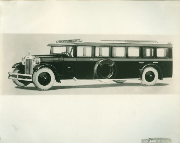 Three-quarter length left side view of a mid-1920s International Harvester Bus. This illustration was possibly used for advertising and catalogs for the International Harvester Company. A spare tire is mounted on the side just behind the driver's side door. The sign on top of the bus reads: "Grand Rapids and Ionia." Presumably Michigan.