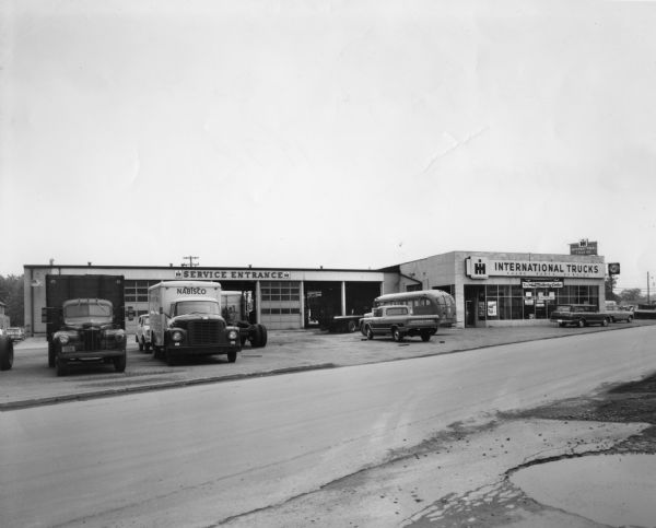 International branch dealership, service entrance side. Various trucks are parked in front, including a Nabisco vendor truck. Original caption on back reads: "Altoona, PA Branch Pittsburgh District MT May 1930."