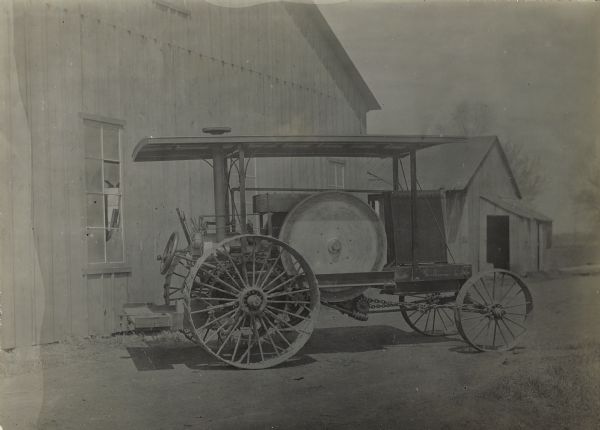 Right side view of a friction-drive tractor parked outdoors in front of a barn.