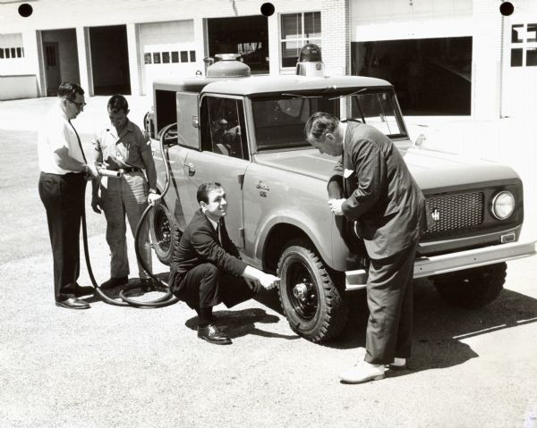 International Harvester Scout fire truck. Original caption reads: "Photograph MW-441-- A fire-fighting adaptation of the Scout by International has been placed in service by Commonwealth of Pennsylvania for use at the state airport serving York and Harrisburg, Pa. Col. Thomas Edward Gurnett (right), manager of state owned airports, watches as International Salesman Ned Pantelich demonstrates the all-wheel drive model's locking hub feature. The hose under discussion at the rear of the Scout is connected to a cylinder in the vehicle's bed that contains 300 lbs. of potassium bicarbonate, a dry chemical fire extinguisher. MT-2677. CR-1146-D."