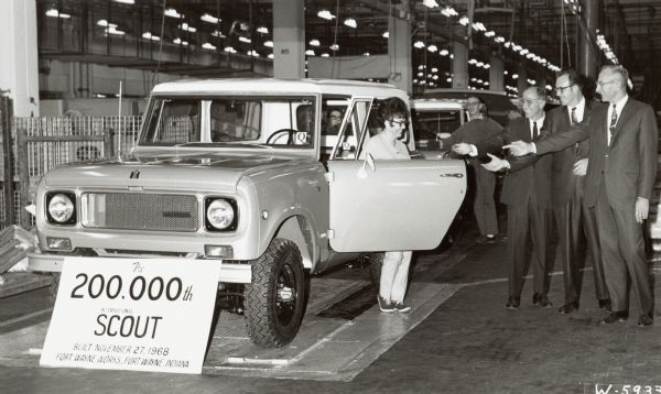 200,000th International Harvester Scout driving off the assembly line at the Fort Wayne Works. Taken inside the plant with a frontal view. Original caption reads, "Photograph W-5933-- Almost eight years to the day after the first one was produced, the 200,000th Scout compact utility vehicle was driven off the assembly line at the Fort Wayne Works of International Harvester Company's motor truck division. In ceremonies heralding the milestone, the Scout is greeted by its new owner, Mrs. June Pontello, an employee at the Works. Mrs. Pontello's Scout is the first of the new models just introduced by International. Sharing the important moment with her are (from left) Homer C. Keck, manager of the Fort Wayne sales branch; R.E. Mills, superintendent of the Scout assembly line at the Works; and H.A. Ehrman, Works manager. MT-3267." Sign reads, "The 200,000th International Scout, Built November 27,1968. Fort Wayne Works, Fort Wayne, Indiana.