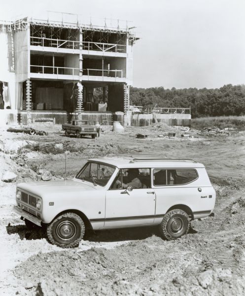 International Harvester Scout in construction site. Original caption reads: "Photo # W-6965-- Scout vehicle from International Trucks offers many construction industry options, such as All-Wheel drive, PTO, winches, several manual transmissions, tow hooks and skid plates. Engines feature high torque, durability. Available in standard trim, in five-seat station wagon traveltop or with similar panel top, and in cab-top pickup version (DeLuxe Traveltop with automatic transmission shown here). MT-3610 (1)." Scout parked in a construction zone, with half-torn building in the background.
