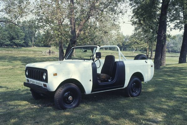 Three-quarter view from front of driver's side. Scout with white panels, and a black panel around the driver's side door. Has a roll bar. Parked outdoors, trees in background.