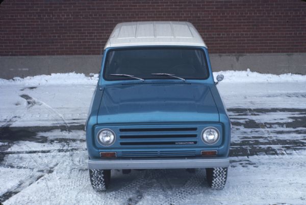 Elevated Front View of Blue Scout with White Top parked in the snow in front of a brick building.