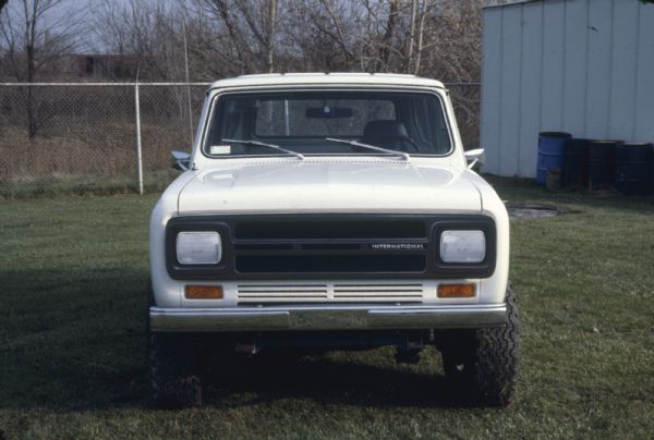 Front view of a white Scout parked on a lawn outdoors. An industrial building is on the right.