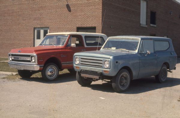 Blue Scout, and red Scout, parked outdoors in front of a brick building.