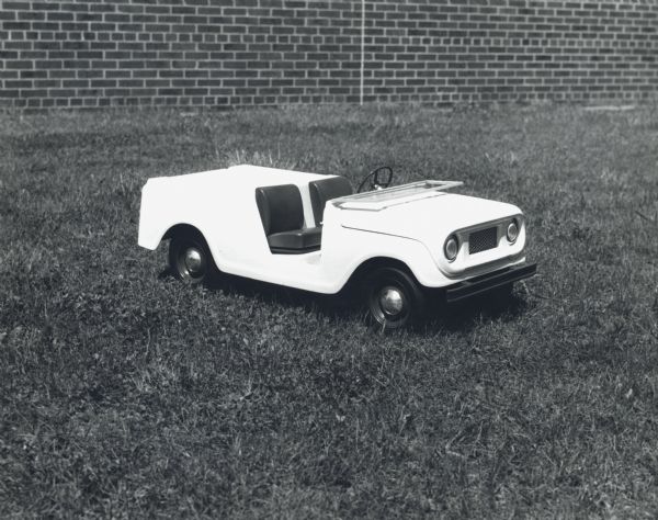 Small scale model of the International Scout. Three-quarter view from front of passenger side of model set in the grass with a brick wall in the background.