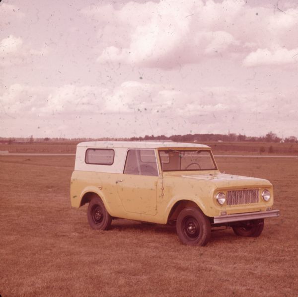 Yellow Scout with white top parked in a large mowed field.