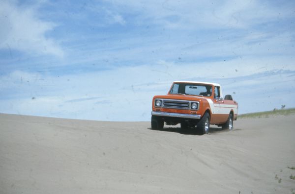 Three-quarter view from front of driver's side of Terra being driven in the sand. Orange with white detailing on side and hood. White cab top. Spare tire is attached inside truck bed.