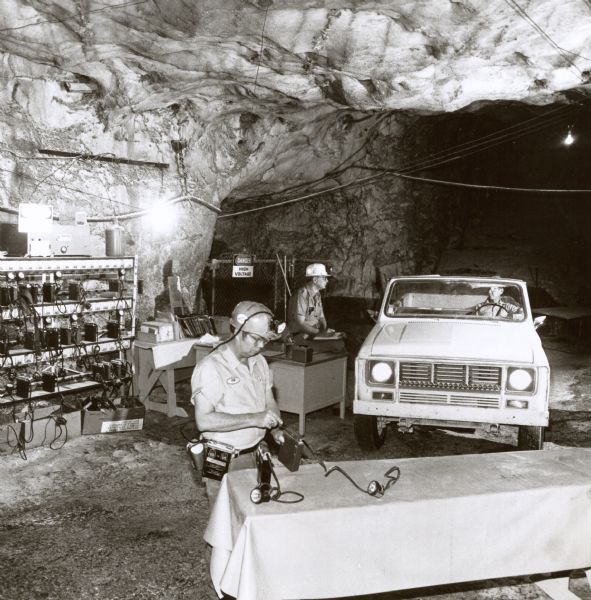 Original caption reads: "(Photo #TF-1540) -- Miner (foreground) at Morton Salt Company's operation near Grand Saline, Tex., services helmet lights as Mine Superintendent J. Ray Rucker (at desk) checks over one of the three diesel-powered International Scout Terra pickups operating in the mine, 750-ft below the surface, to serve as a personnel carrier, handle small loads or tow mining equipment on skids. TD-4029. 6/6/77"