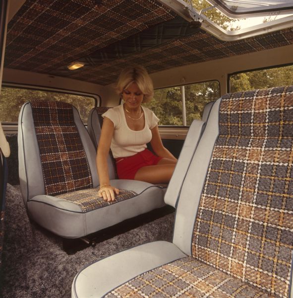 Interior view of woman sitting in passenger seat of Scout. Grey seats with plaid fabric.
