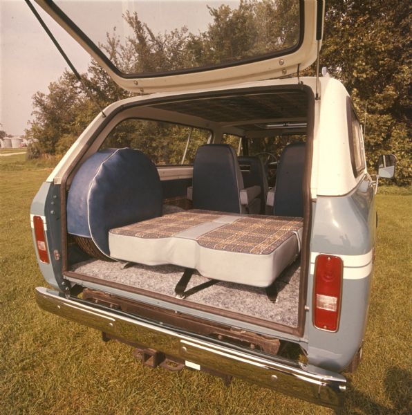 Rear view of Scout. Hatchback is open, spare tire is attached to inside of truck and has a blue cover. Back seat is folded down, revealing plaid upholstery. According to Jim Allen, this third row seating became a bed when folded down. See note below. 