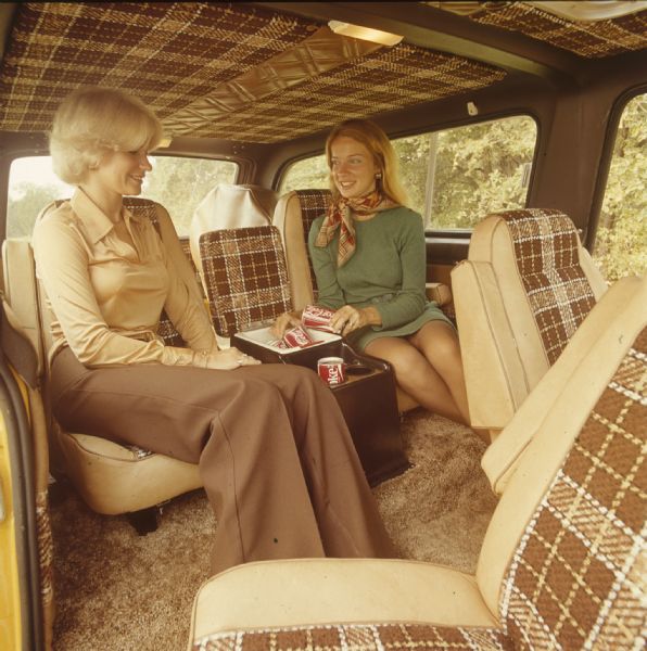 View across front passenger seat, which is swiveled to the side, of two women sitting in the middle passenger seats of a Scout. Between them is a cooler filled with Coca-cola.