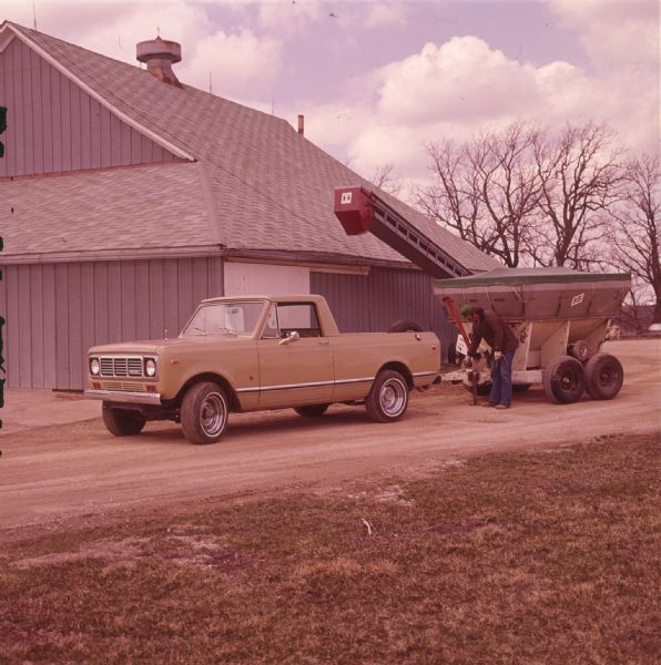 Man attaching agricultural machinery to a Scout parked near a barn.