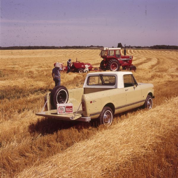 Scout Terra parked in a field with a box of baler twine sitting on the top of the open tailgate. A man is walking behind the Scout carrying a package of baler twine towards another man in the background who is working on agricultural machinery attached to a tractor.