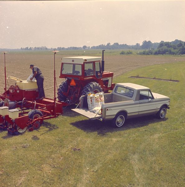 Elevated view of Scout Terra parked in a field. Next to the Terra a man is pouring the contents of a bag into agricultural machinery attached to an International tractor.