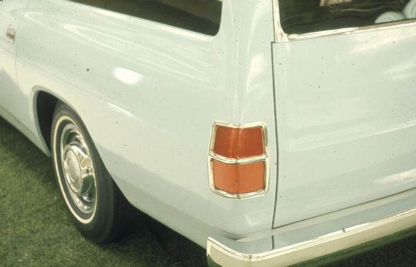 Detail of light blue Scout Wagon rear tire and tail lights on driver's side. Partial view of double doors on back. Parked indoors on synthetic carpeting that looks like grass.