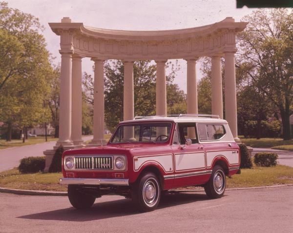 Three-quarter view from front of driver's side of red Scout II Traveltop parked outdoors. Behind the Scout is a semi-circle columned monument on a grassy median between two streets, in what appears to be a residential area.