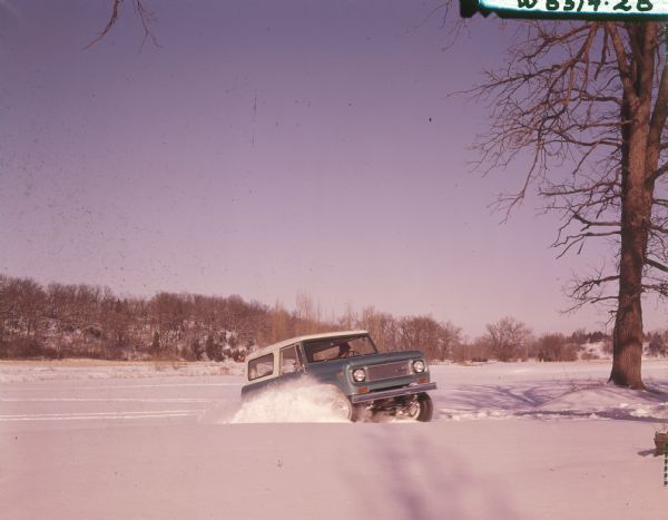 Blue Scout being driven through deep snow. There may be a frozen lake in the background.