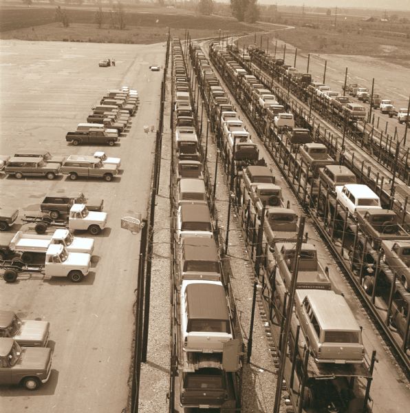 Elevated view from rear of railhead. Trucks are parked on the left and right, alongside the "Texas Special" train load of light duty vehicles which are on five railroad tracks. The vehicles are loaded double-decker style.