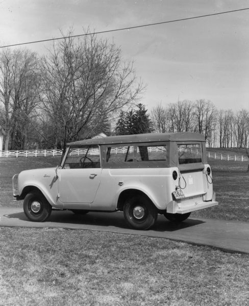 Driver's side view of soft-top covered wagon parked outdoors. Insignia on side panel reads: "Scout." License plate on back reads: "Truck 1961 Ohio." A white fence and trees are visible in the background.