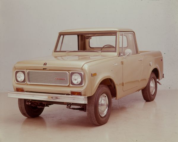 Three-quarter view from front of driver's side of yellow Scout with truck bed parked indoors.