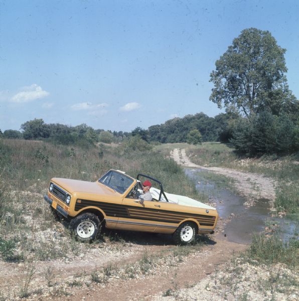 Man driving Scout Terra on a gravel road near a stream.
