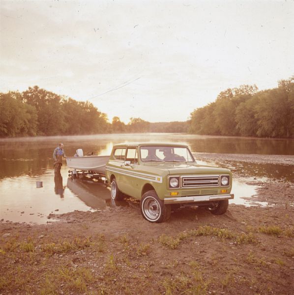 Two men with Scout at a boat launch. One man is driving, and the other man is wearing waders and is standing in the water holding the back of the boat. The boat is on a trailer attached to the Scout.