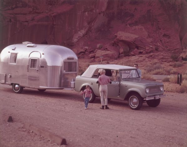 A man, woman, and young child standing outside a Scout 810 convertible. They are parked on a road near a sign that reads: "Petroglyphs." The Scout is pulling an Airstream travel trailer.