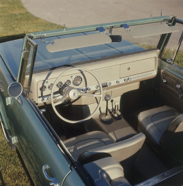 View looking down at interior of driver's side of blue International Scout 800 parked outdoors on the grass.