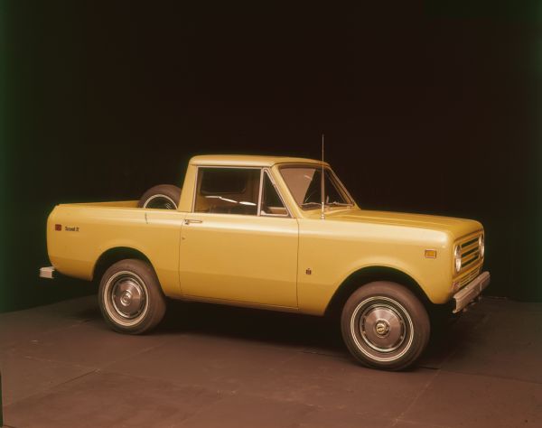 Passenger side view of yellow Scout II pickup, with a spare tire mounted on the inside of the truck bed.
