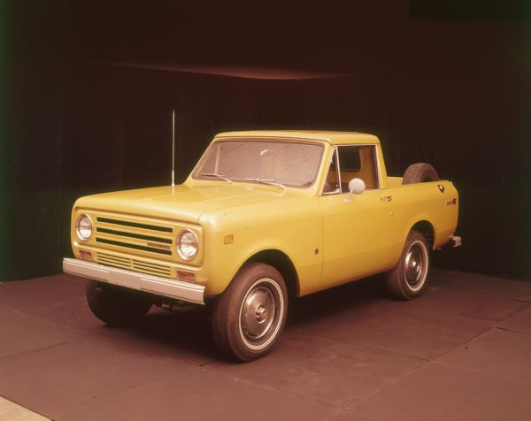 Three-quarter view from front of driver's side of yellow Scout II pickup truck. Spare tire is mounted on the inside of the truck bed.