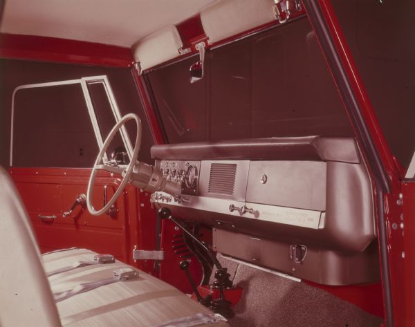 Interior view, from open door on the passenger side, of front seat, steering wheel and dashboard of red International Scout 800 pickup. The driver's side door is also open.