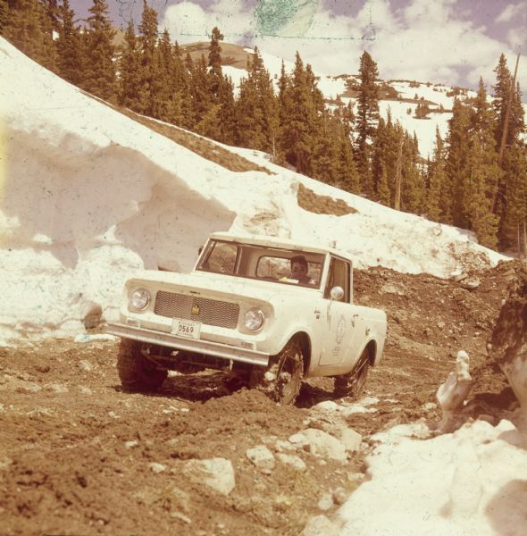 View from front of man driving up a hill surrounded by snow in a mountainous area.