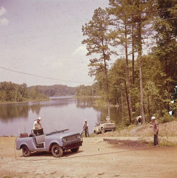 Group of men (some in hardhats) working near the edge of a lake with two Scouts. There are trees and a small lake in the background.